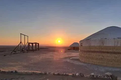 Sunset over Ayaz Kala fortress with traditional yurts and camel riders in the Kyzylkum Desert, Uzbekistan