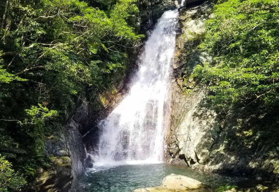 Tall cascading Hiji Falls waterfall flowing into a deep pool surrounded by tropical jungle