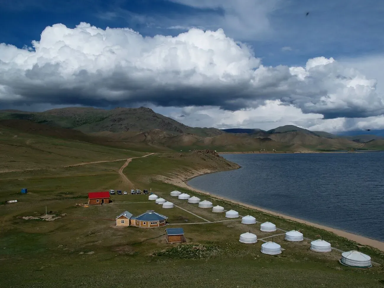 Traditional Mongolian ger camp settlement on the grassy shores of White Lake surrounded by rolling green hills under a blue sky