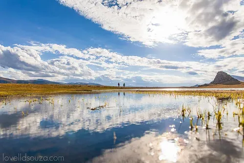 Two travelers standing at the edge of White Lake in Mongolia with dramatic clouds reflecting perfectly on the still turquoise water surface