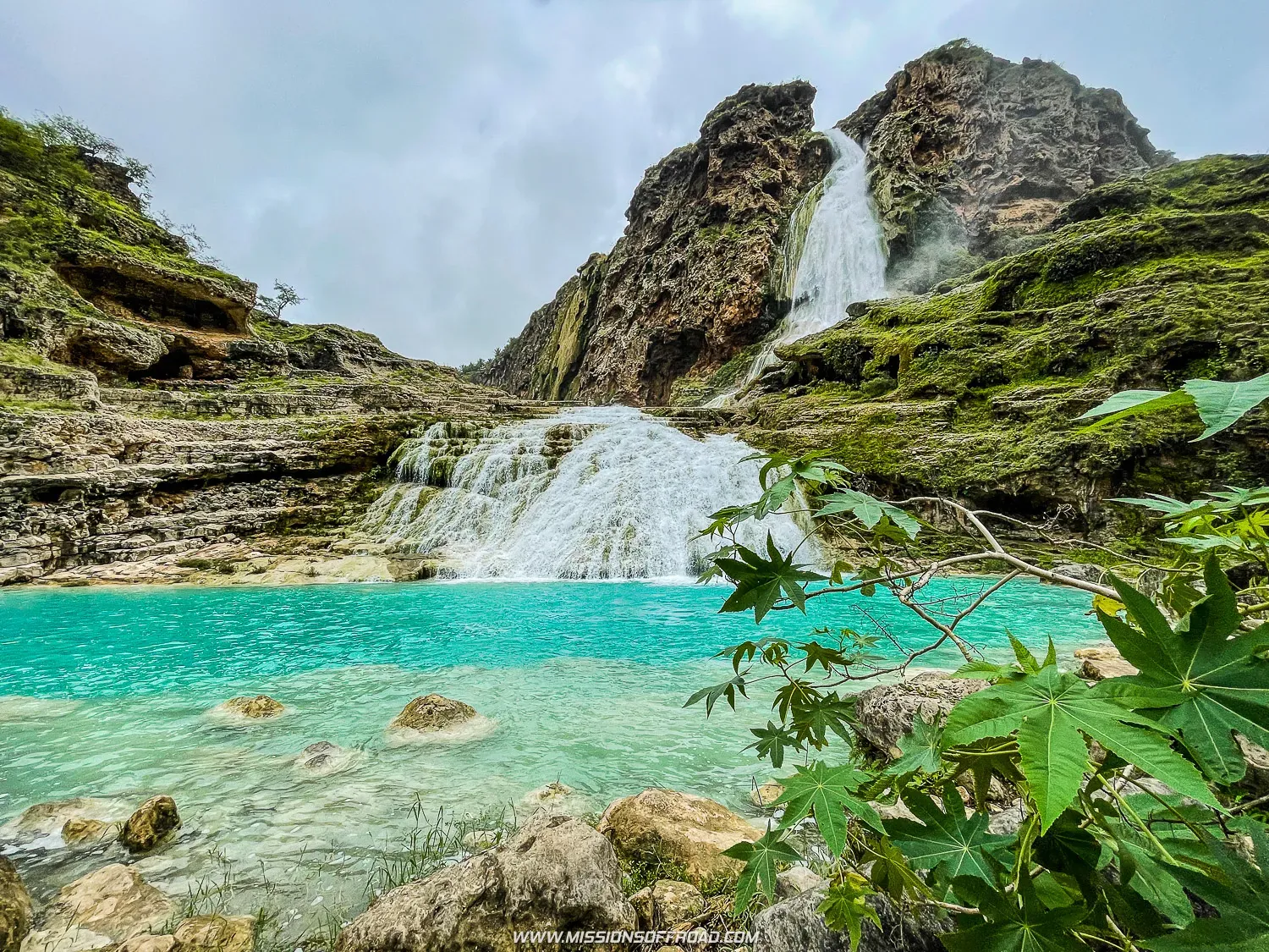 Travertine curtain formation at Wadi Darbat waterfall with water flowing over layered rock deposits