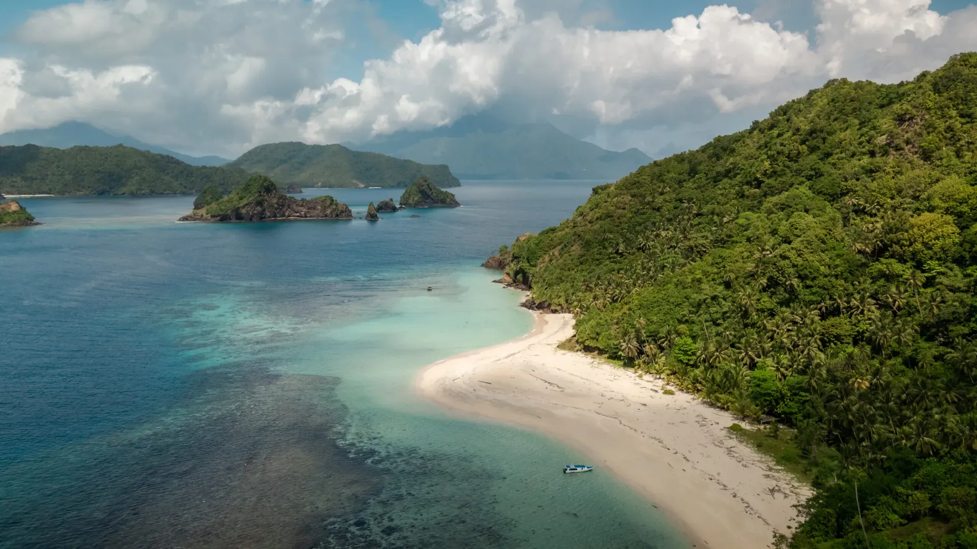 Tropical beach with white sand and turquoise water on Siau Island with Mount Karangetang volcano in the background, Indonesia