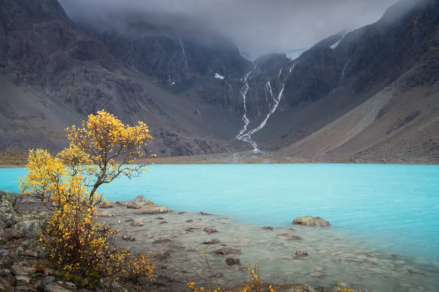 Turquoise Blåisvatnet lake with waterfalls flowing from the Lenangsbreen glacier down dark mountain faces