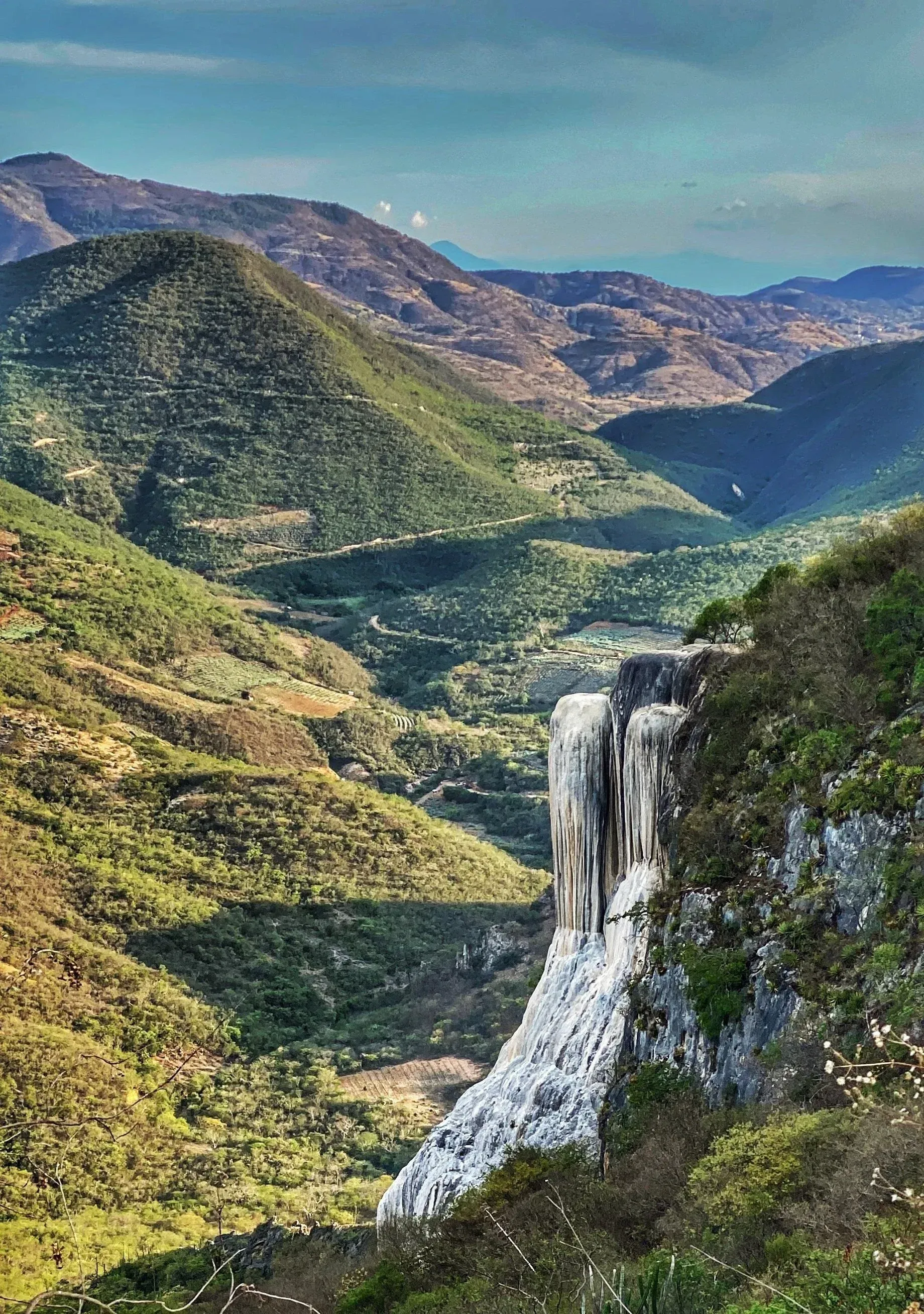 Two massive petrified waterfalls cascading through lush green valley in Sierra Madre mountains at Hierve el Agua Oaxaca Mexico