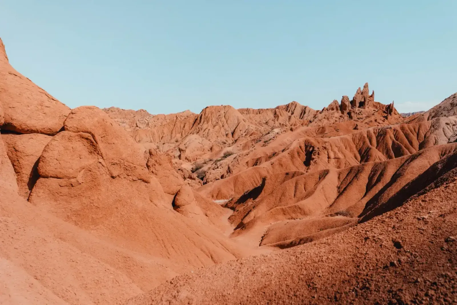 Orange-red rock formations and rugged hills of Skazka Canyon under a clear blue sky on Issyk-Kul's southern shore