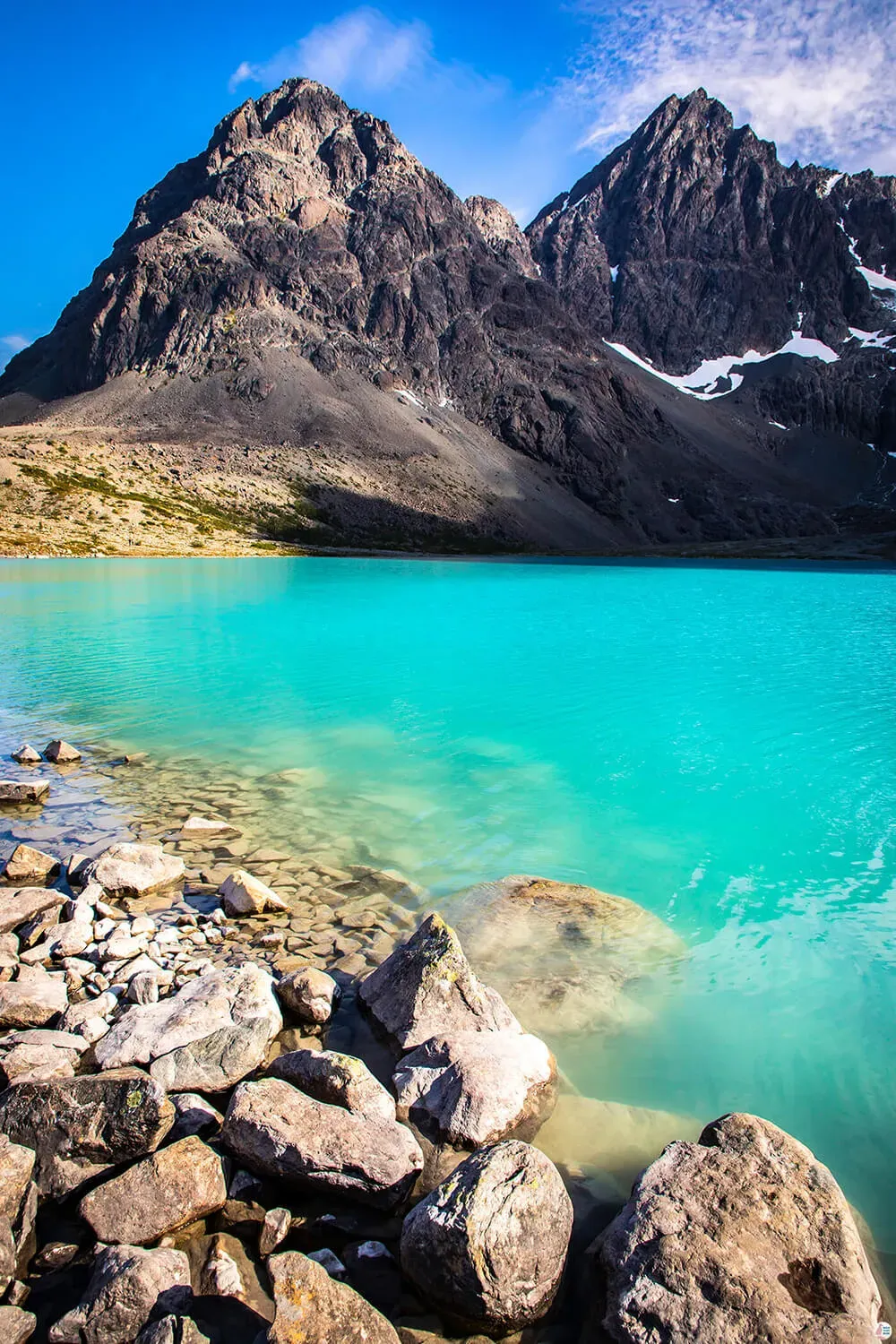 Turquoise Blåisvatnet lake at the base of dark mountains with patches of lingering snow