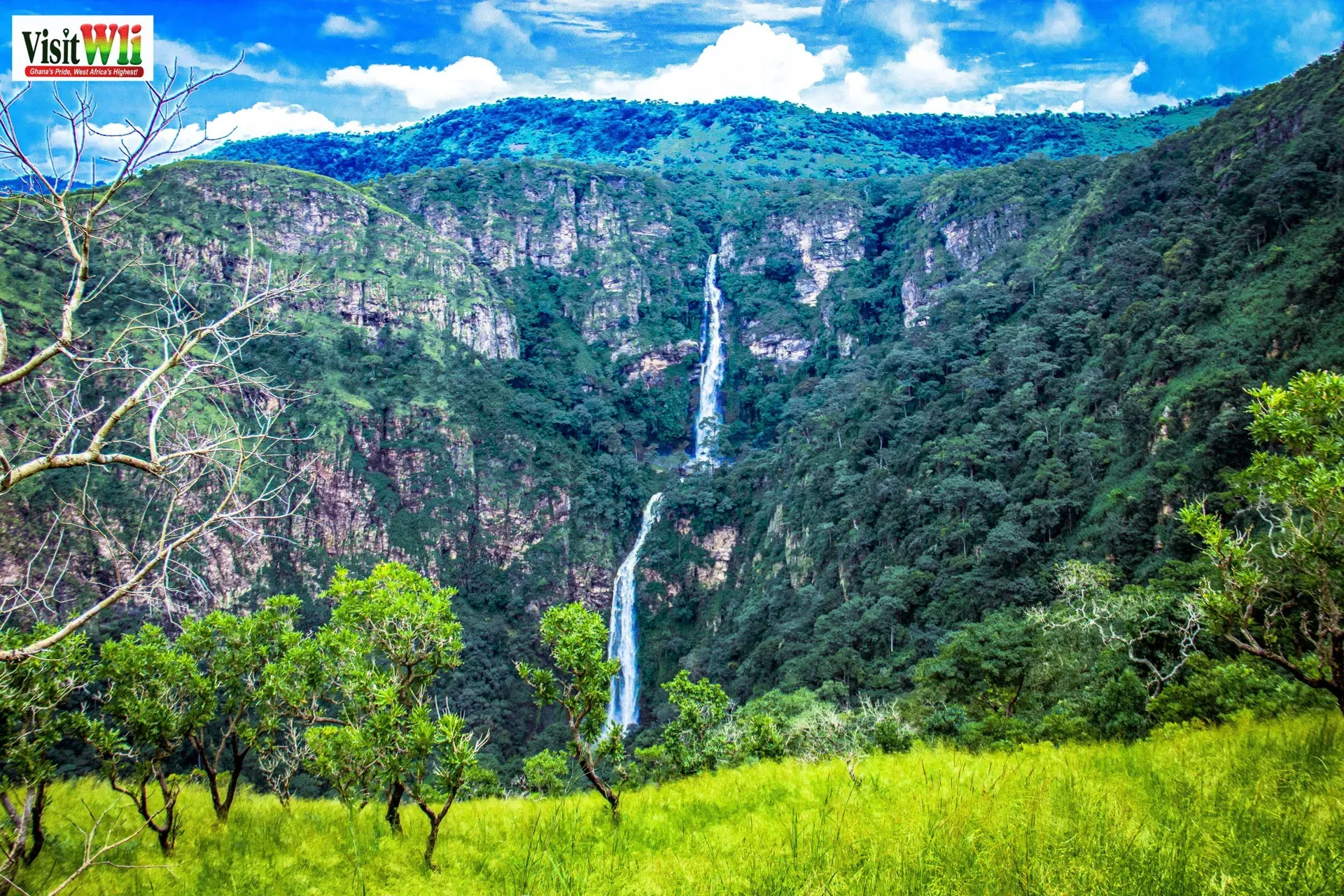 Wli Waterfalls framed by green mountains and bright blue sky