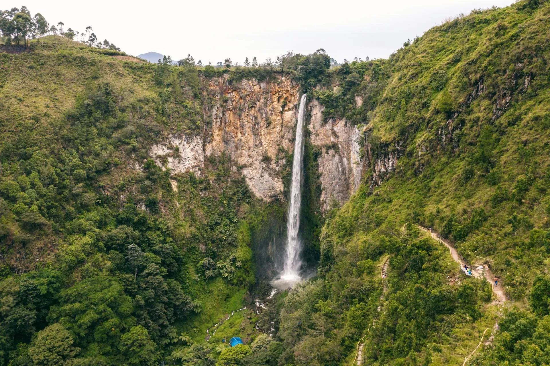 Aerial drone view of Sipiso Piso Waterfall descending from a volcanic cliff into a forested valley