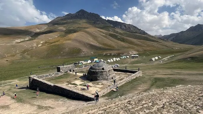 Aerial view of the Tash Rabat caravanserai, a 15th-century stone structure in a green valley surrounded by the Tian Shan mountains in Kyrgyzstan