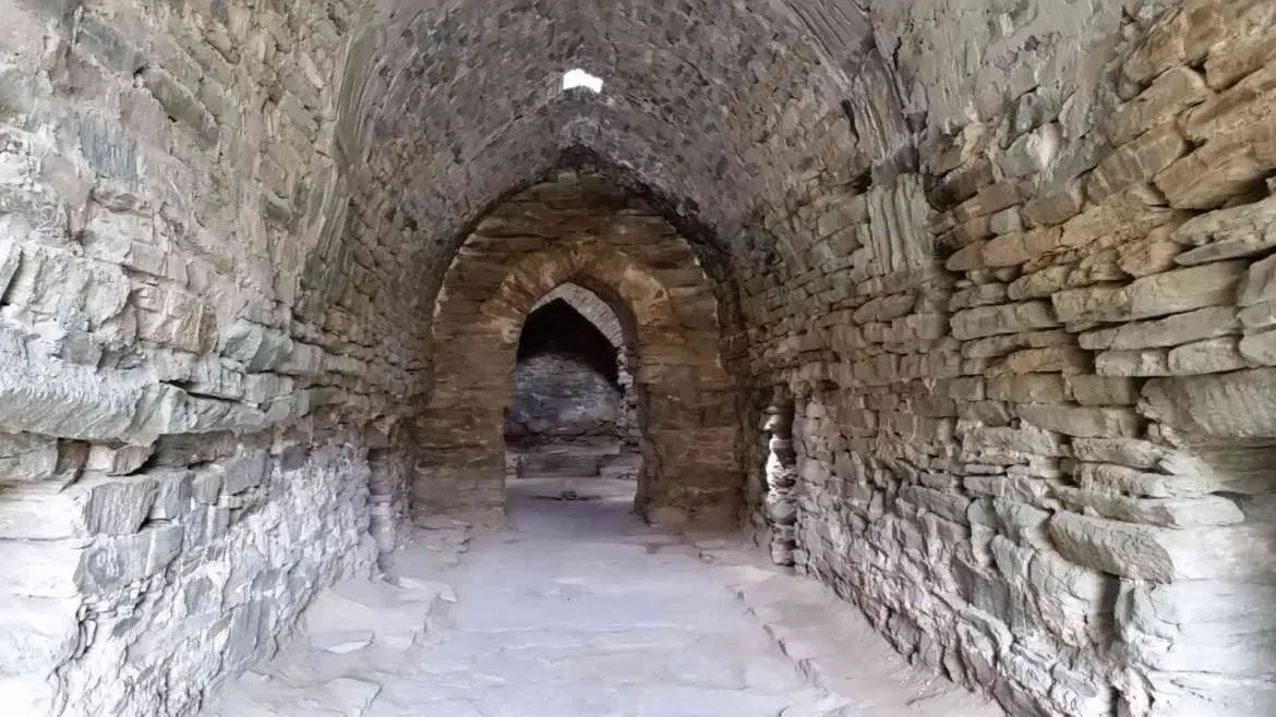 Dark stone interior corridor inside the Tash Rabat caravanserai in Kyrgyzstan, with small openings letting in narrow shafts of light