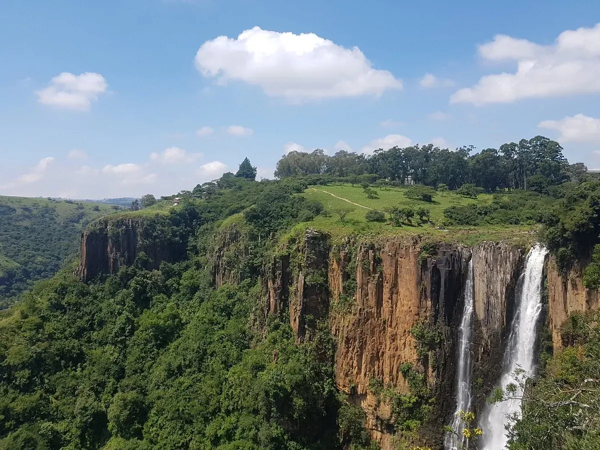 Lush green KwaZulu-Natal Midlands landscape surrounding Howick Falls South Africa with blue sky and white clouds