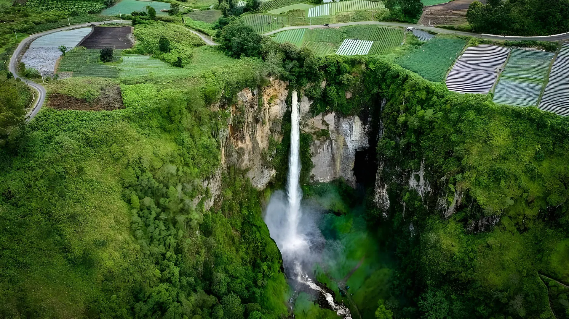 Sipiso Piso Waterfall cascading down rugged cliffs into a green valley with terraced fields