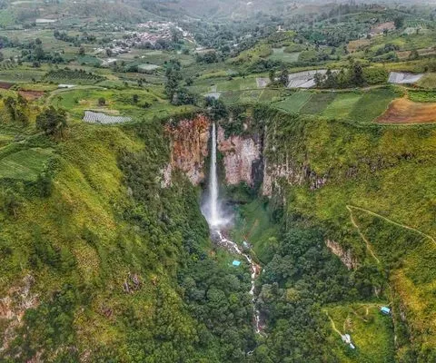 Sipiso Piso Waterfall cascading into a lush green valley near Lake Toba surrounded by terraced fields