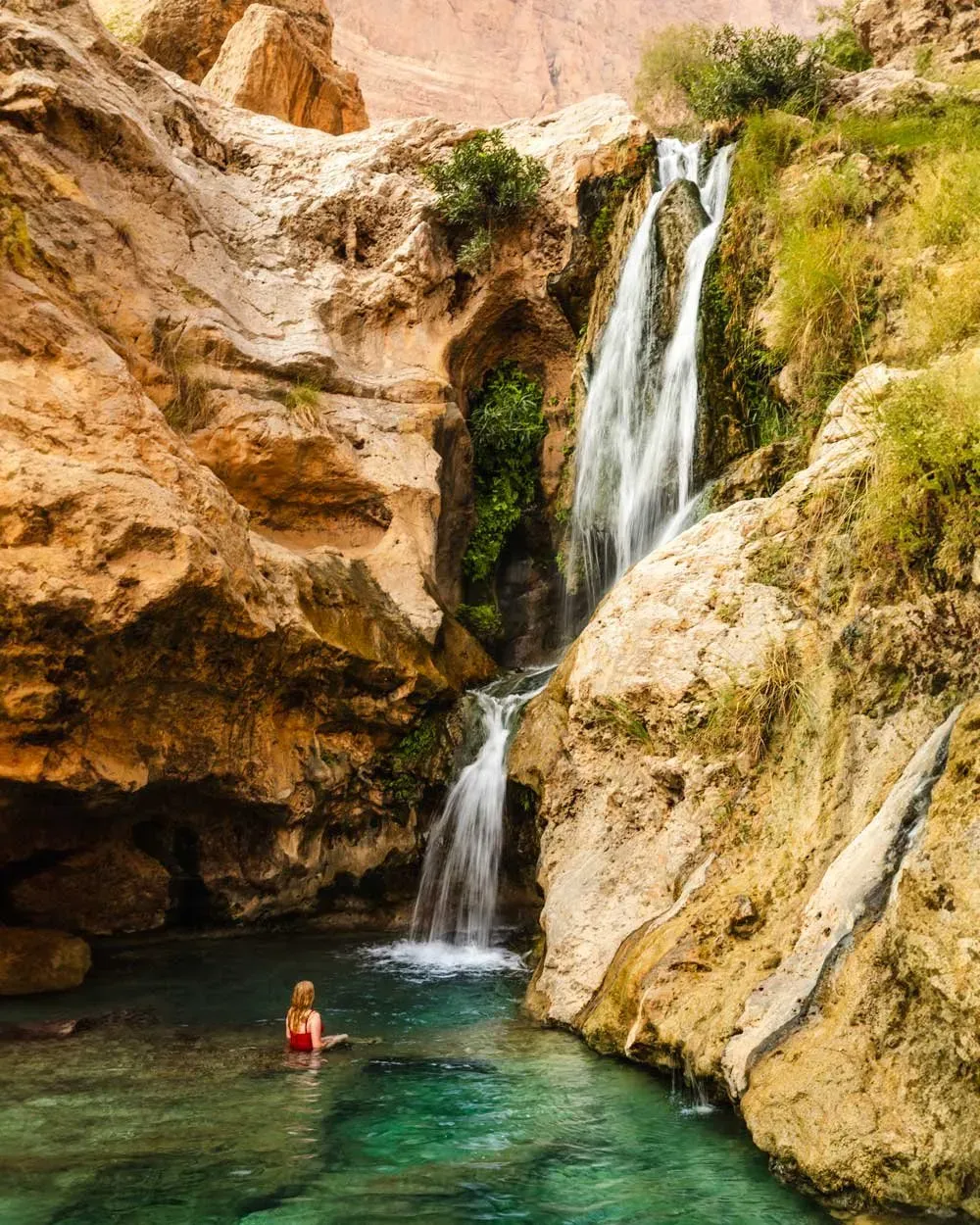 Turquoise pool beneath a cascading waterfall in Wadi Tiwi with dramatic sunlit rock formations