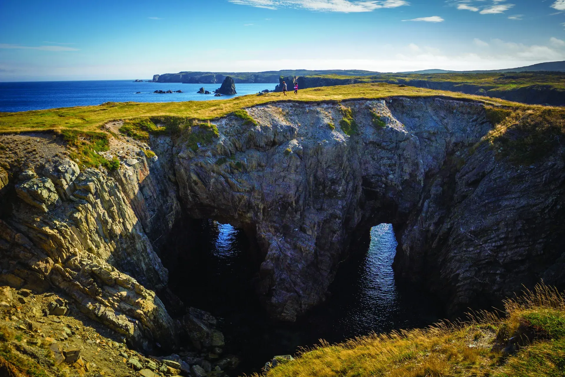 Hikers walking the cliff edge trail above the natural sea arch at The Dungeon Bonavista Newfoundland