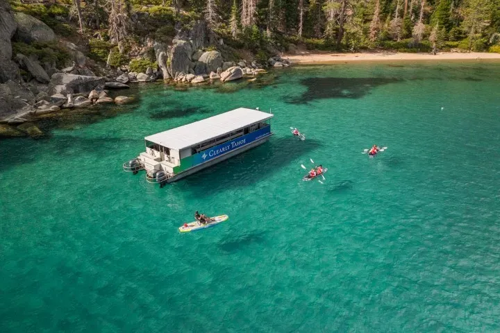 Panoramic view of Lake Tahoe's crystal clear blue waters in California, surrounded by lush green forests with boats on the lake