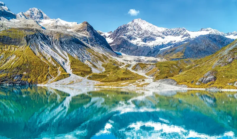 Panoramic view of snow-capped mountains and glaciers reflecting in calm turquoise waters at Glacier Bay National Park