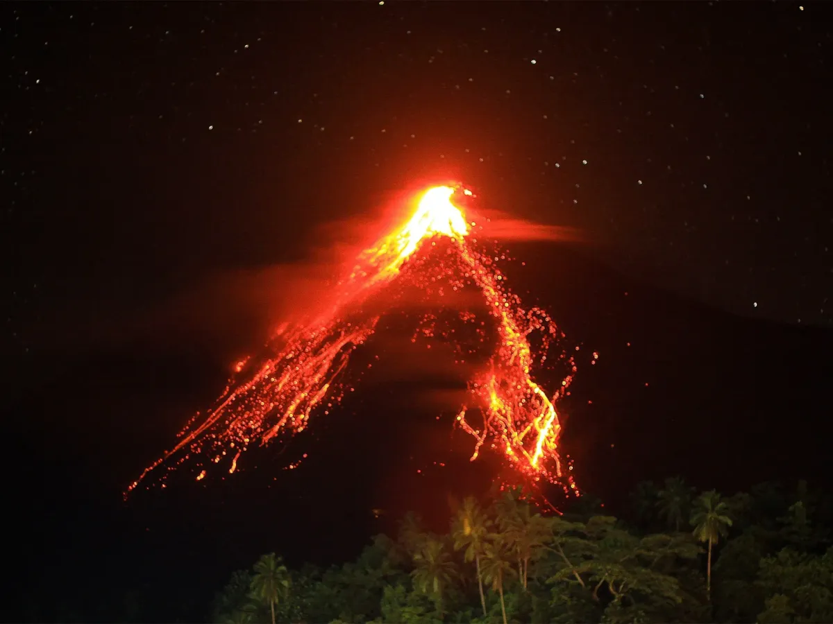 Mount Karangetang volcano erupting at night with bright lava streams illuminating the dark sky over Siau Island, Indonesia