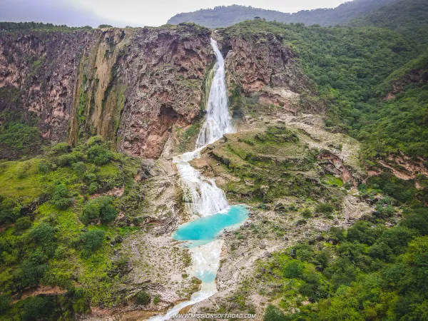 Aerial view of Darbat Steps Waterfall cascading into a turquoise pool surrounded by dense green vegetation in Dhofar, Oman