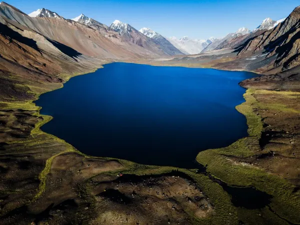 Aerial view of deep blue Karambar Lake Pakistan among rugged snow-capped mountains and green alpine slopes
