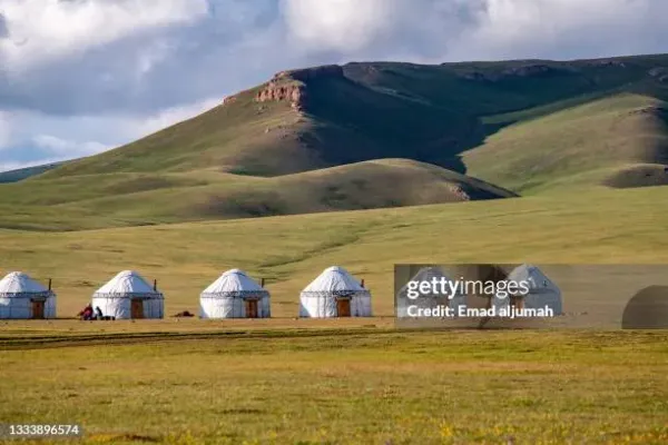 Panoramic view of Song Kol Lake Kyrgyzstan with turquoise water, green summer pastures and snow-capped Tian Shan mountains