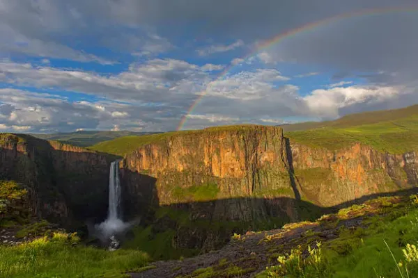 Boalathapo Falls cascading into a lush green canyon with a rainbow arcing across the sky in Lesotho's highlands near Semonkong