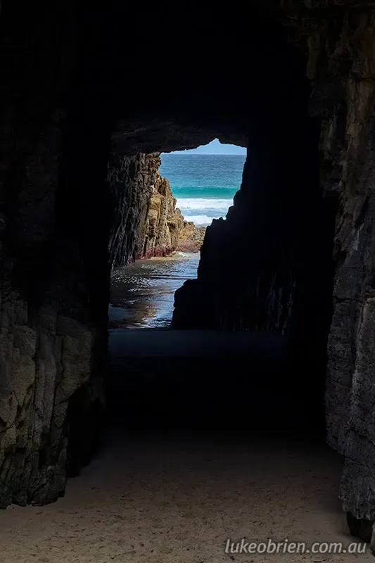 Looking through the dark rocky opening of Remarkable Cave Tasmania out to turquoise Southern Ocean waters on the Tasman Peninsula