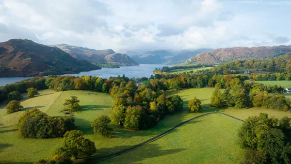 Aerial view of Ullswater lake with golden autumn foliage surrounding Aira Force waterfall and Gowbarrow Fell in the Lake District