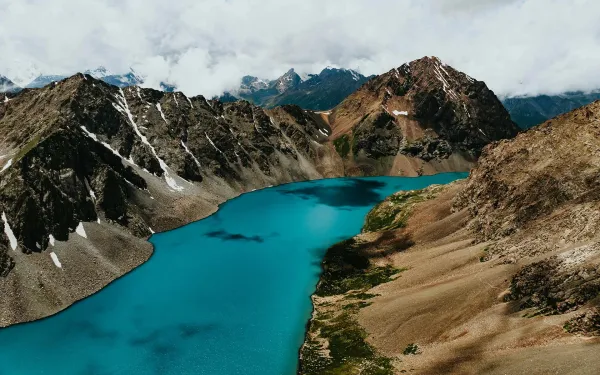 Ala-Kul Lake Kyrgyzstan: turquoise glacial waters surrounded by snow capped Tien Shan peaks under dramatic clouds